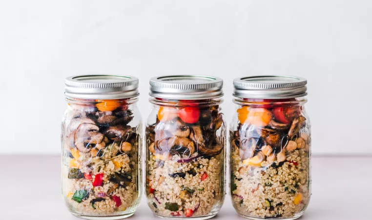 Mason jars filled with healthy food options like quinoa and peppers and mushrooms.